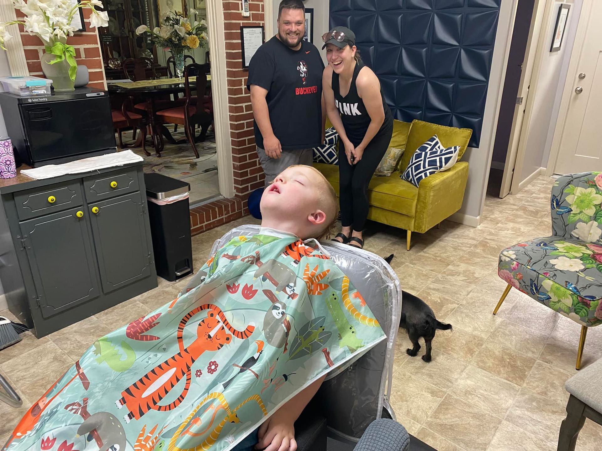 A young boy is laying in a chair getting his hair cut in a salon.