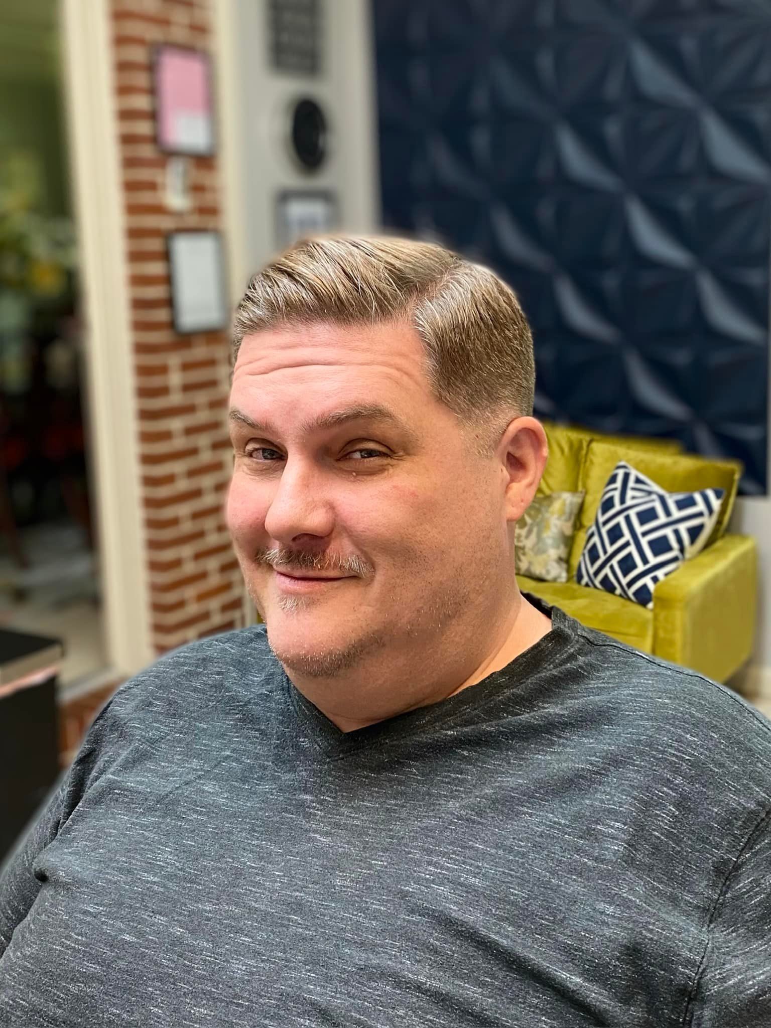 A man with a mustache is sitting in a chair in a barber shop.