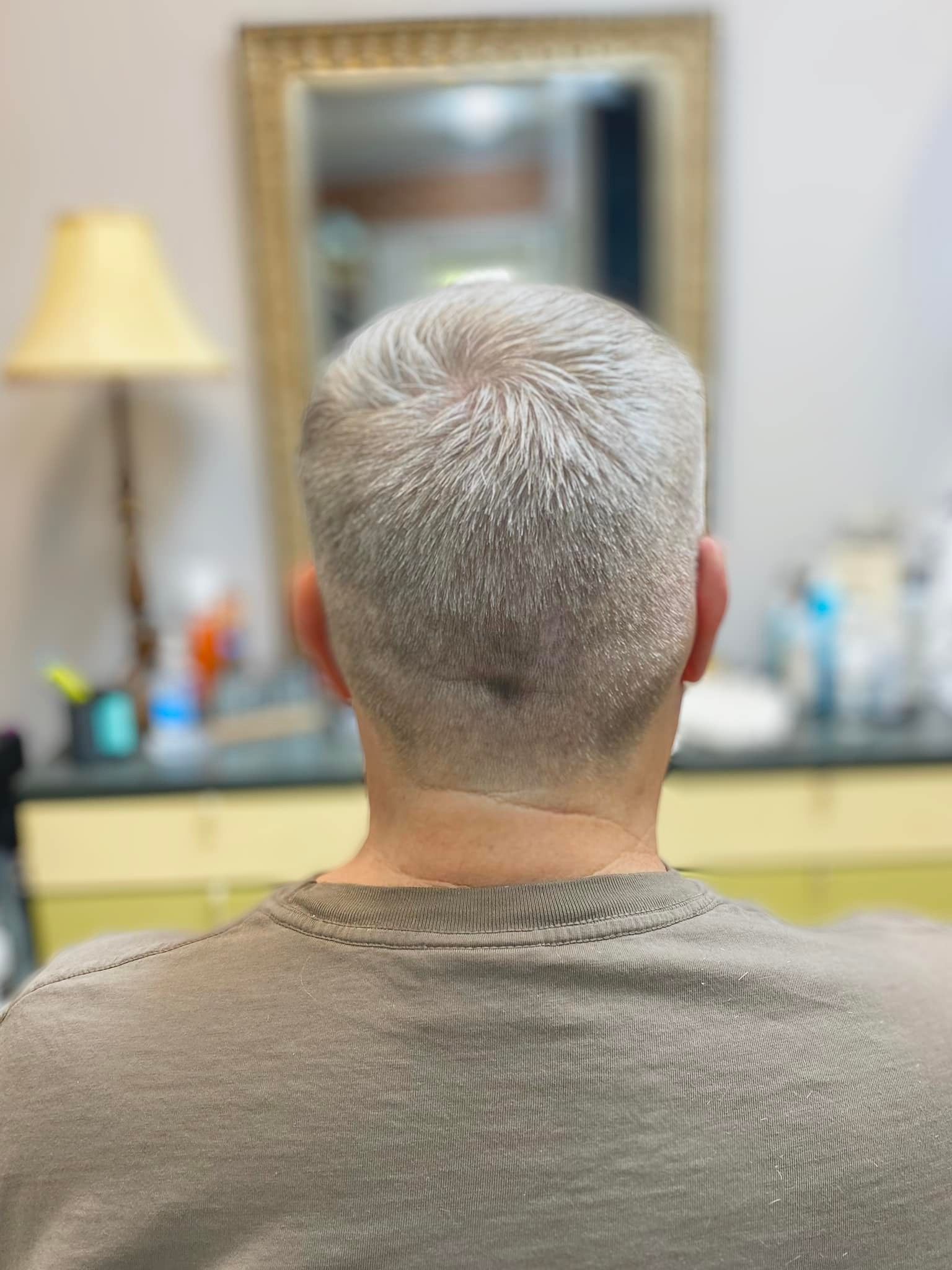 A man with gray hair is sitting in front of a mirror.