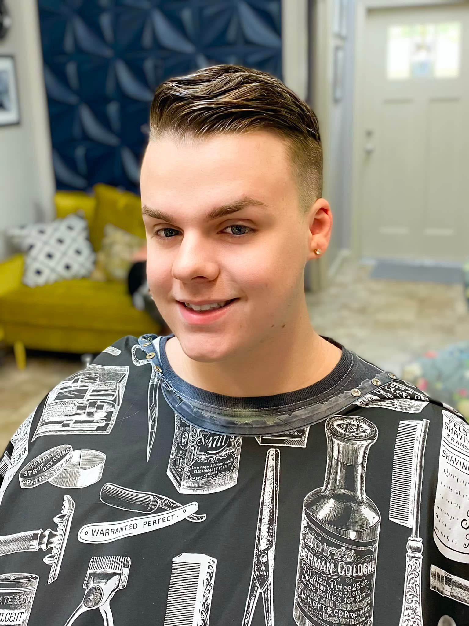 A young man is wearing a black and white shirt with a pattern of barber tools on it.