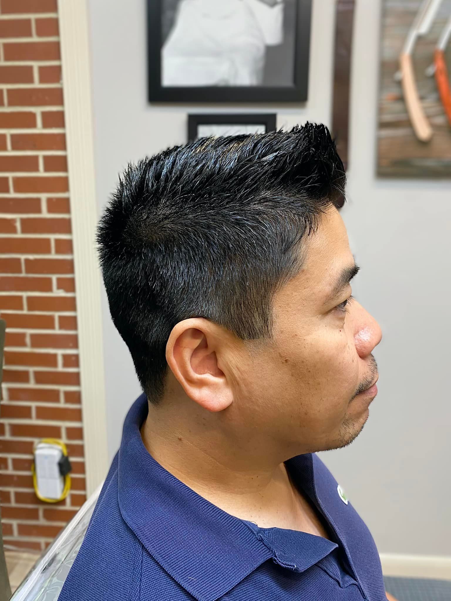 A man in a blue shirt is getting his hair cut at a barber shop.