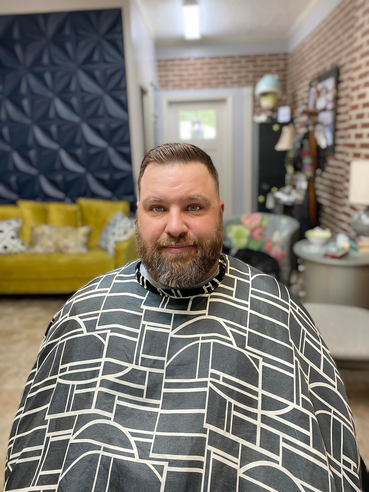 A man with a beard is wearing a cape in a barber shop.