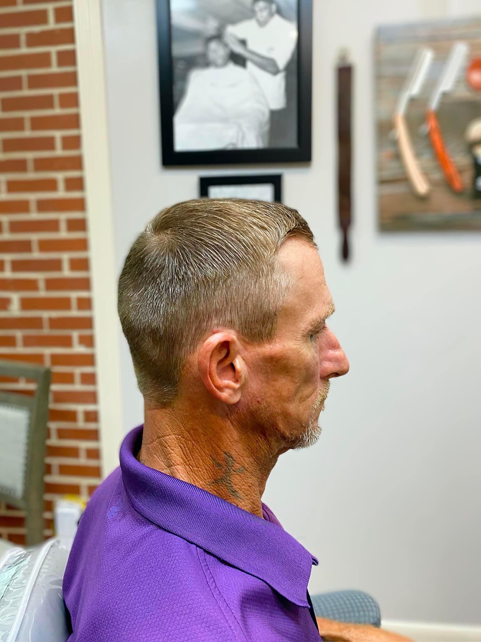 A man in a purple shirt is getting his hair cut at a barber shop.