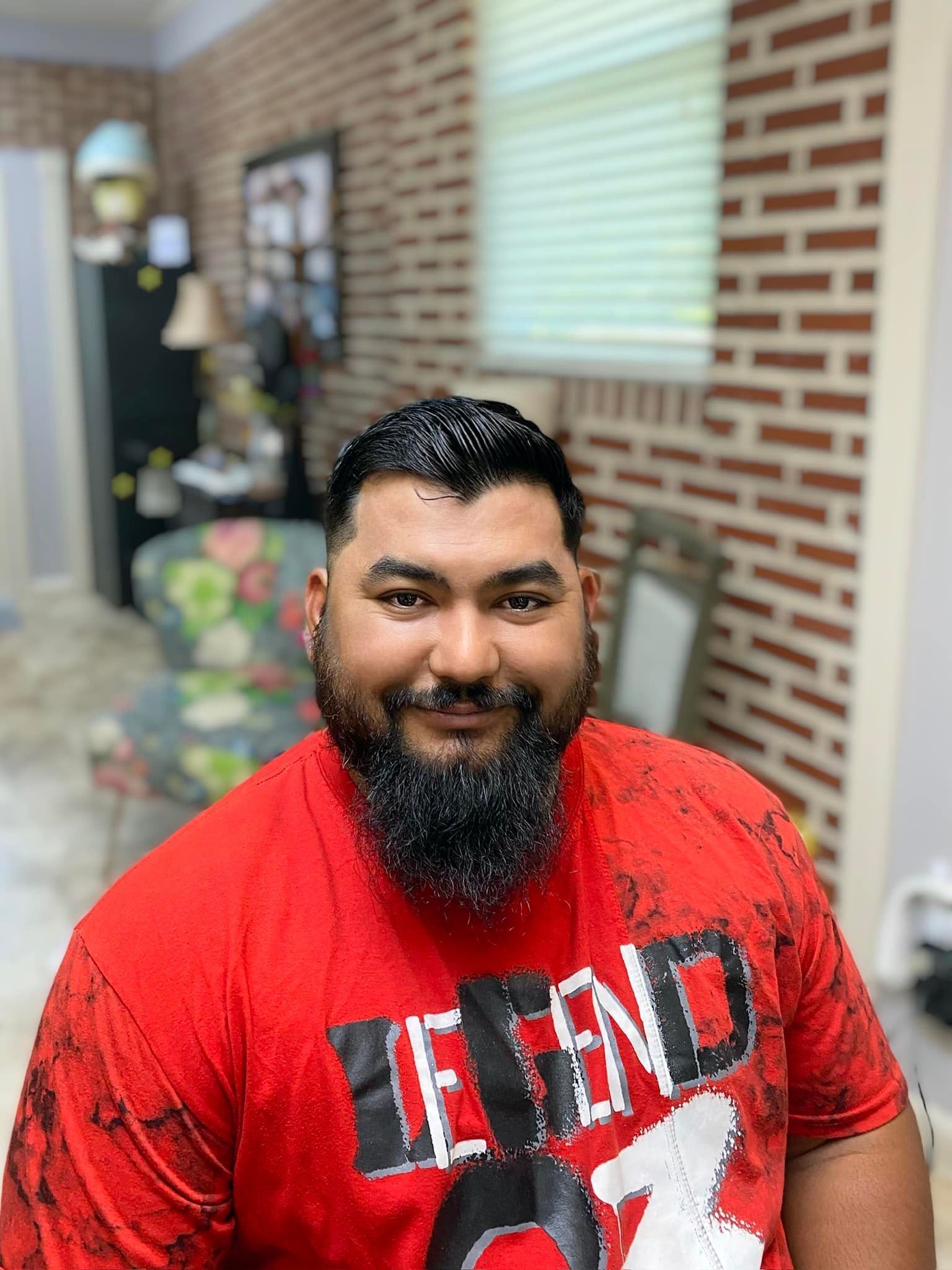 A man with a beard is wearing a red shirt and smiling.