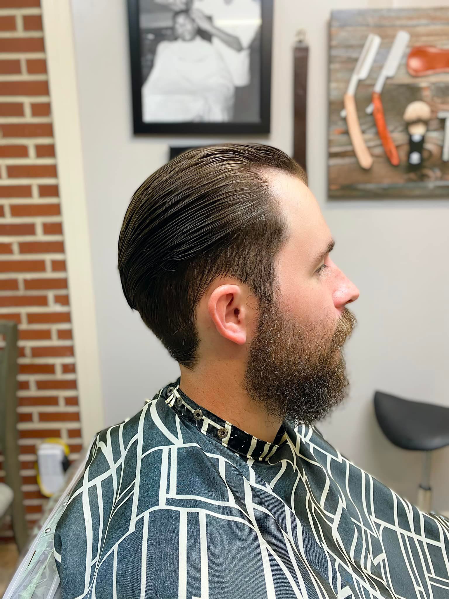 A man with a beard is getting his hair cut at a barber shop.