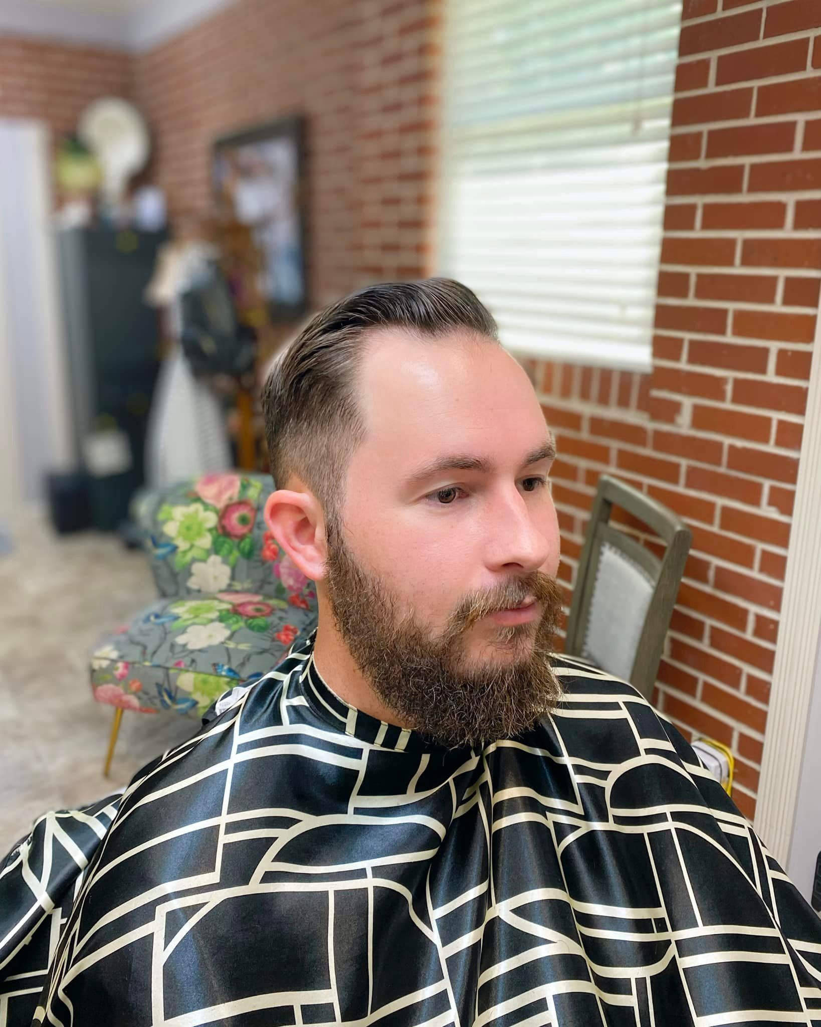 A man with a beard is getting his hair cut at a barber shop.