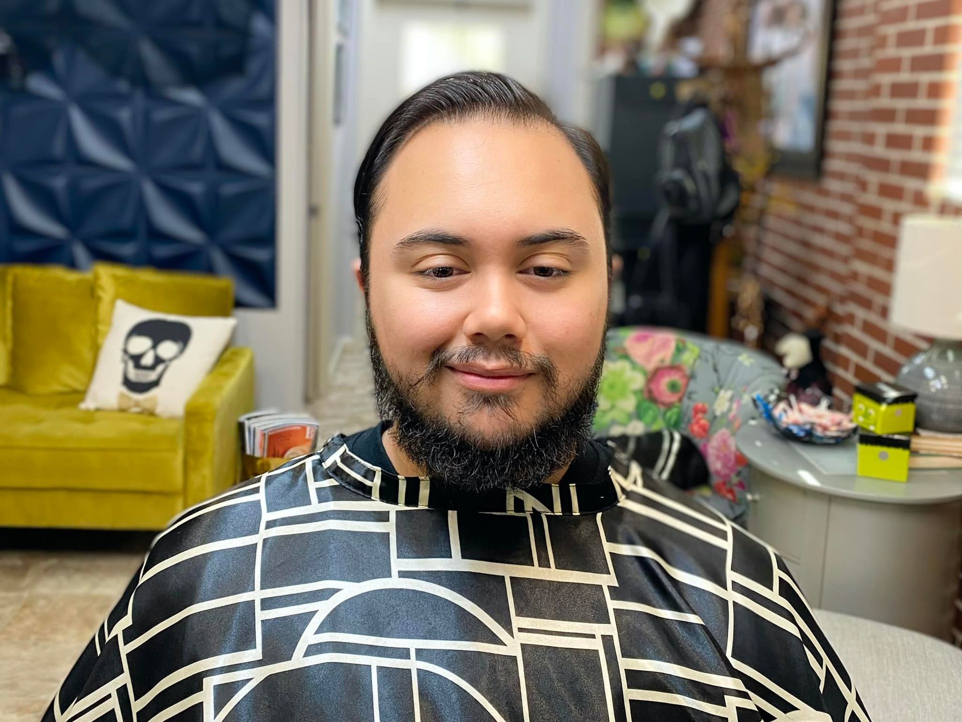 A man with a beard is sitting in a chair wearing a cape.