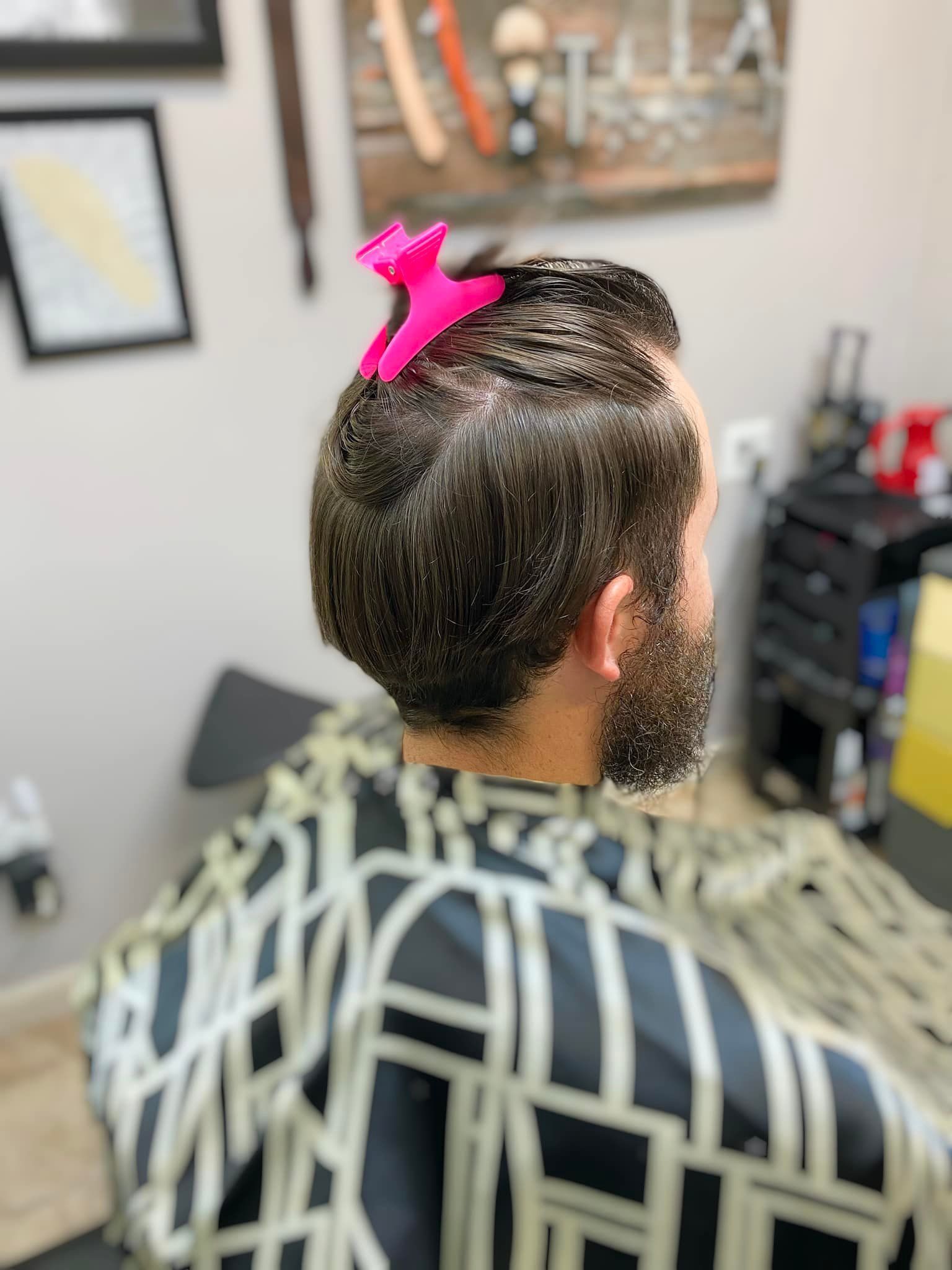 A man with a beard is getting his hair cut at a barber shop.