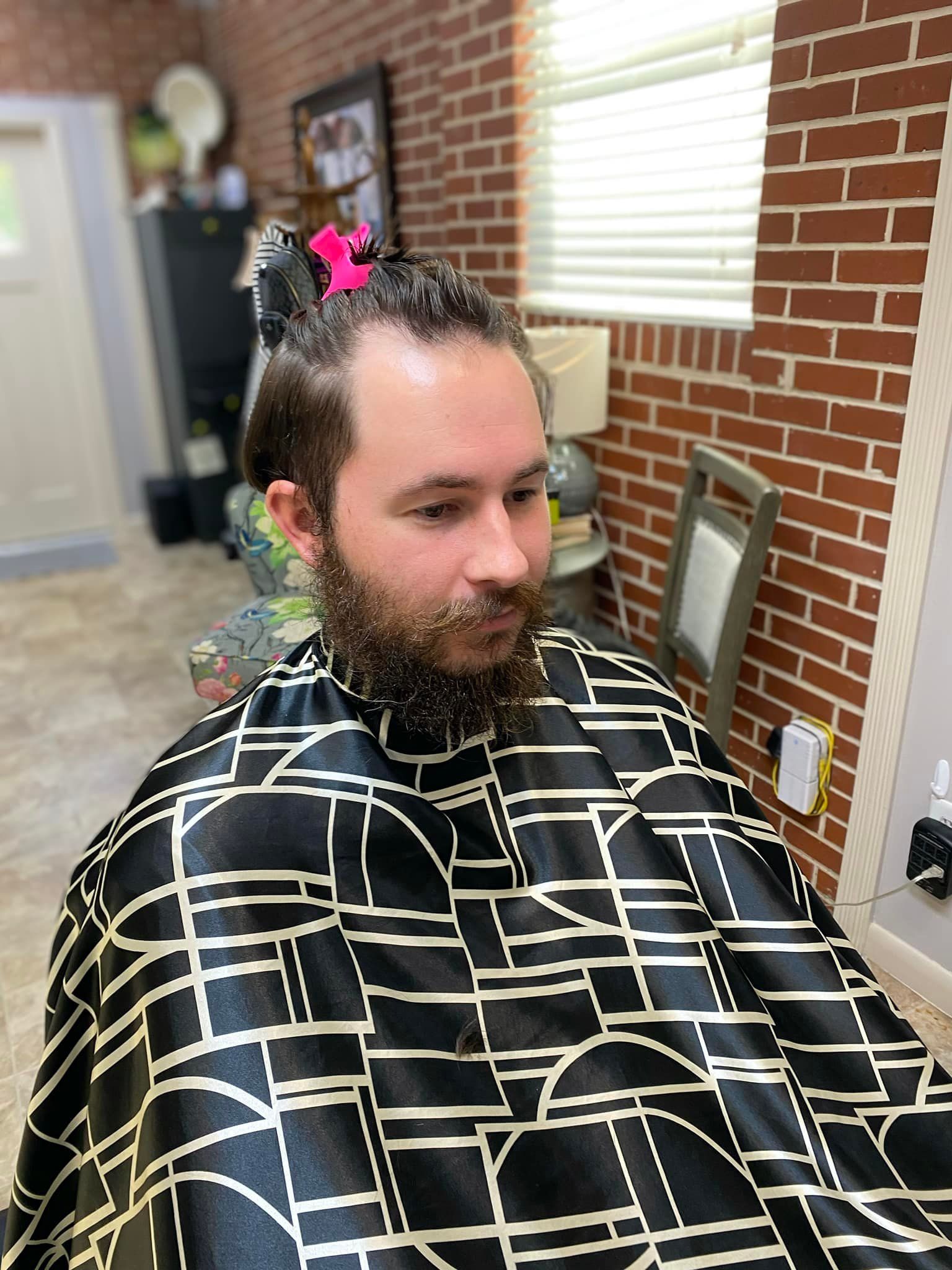 A man with a beard is getting his hair cut at a barber shop.
