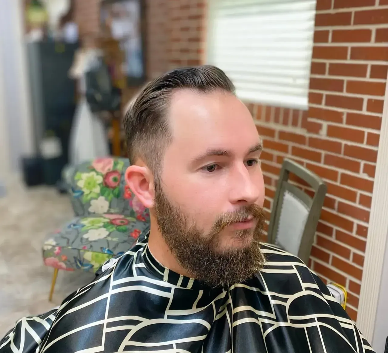 A man with a beard is getting his hair cut at a barber shop.