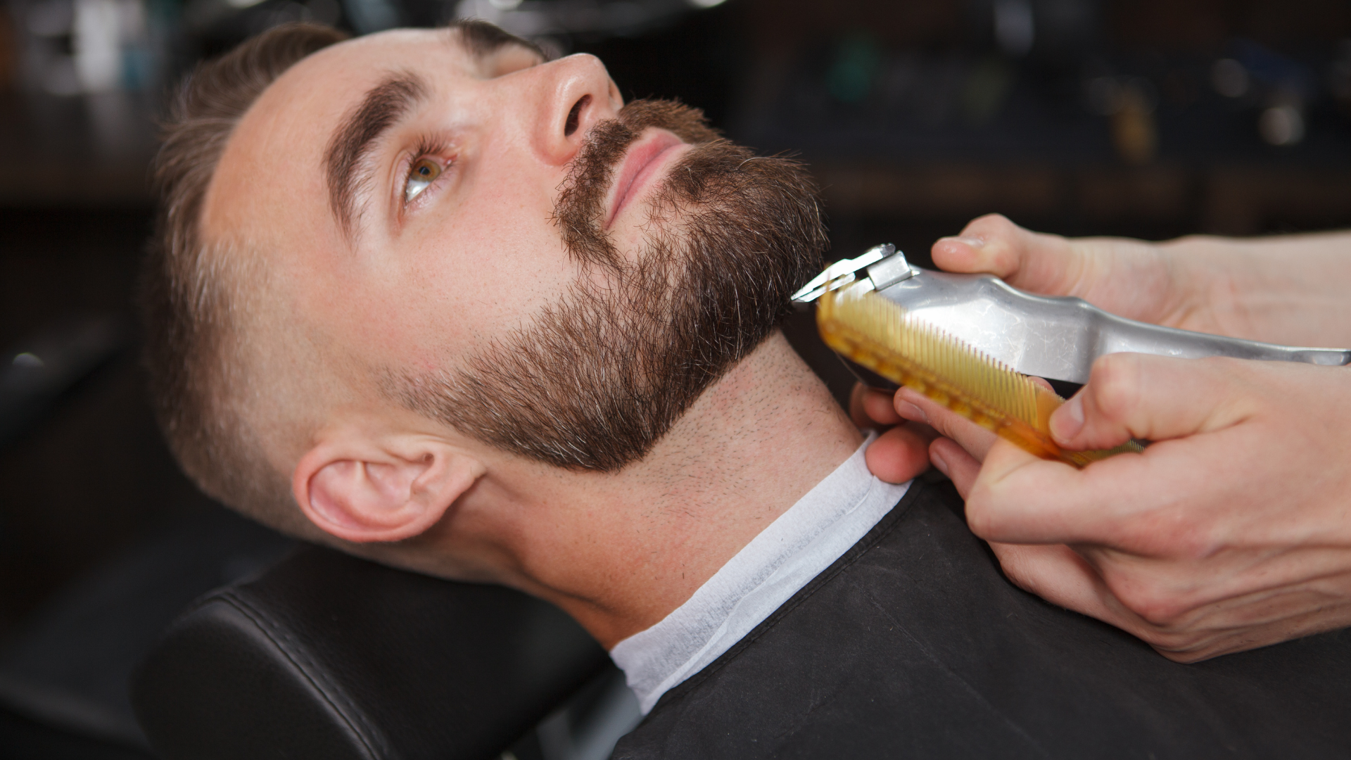 A man is getting his beard trimmed at a barber shop.