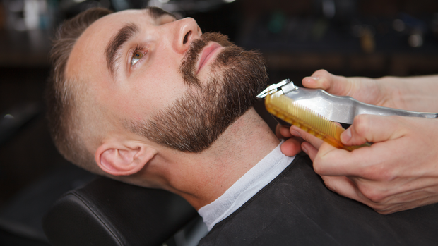 A man is getting his beard trimmed at a barber shop.