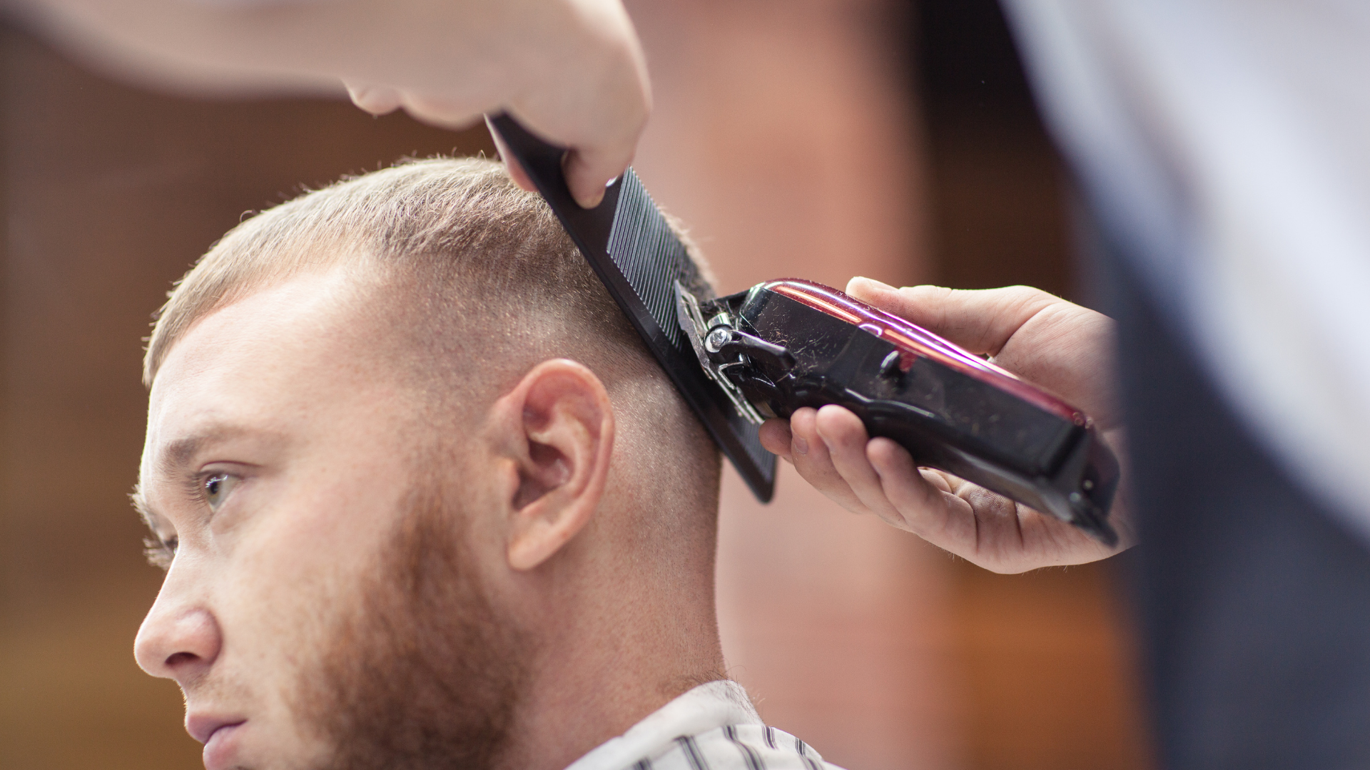 A man is getting his hair cut by a barber with a clipper.