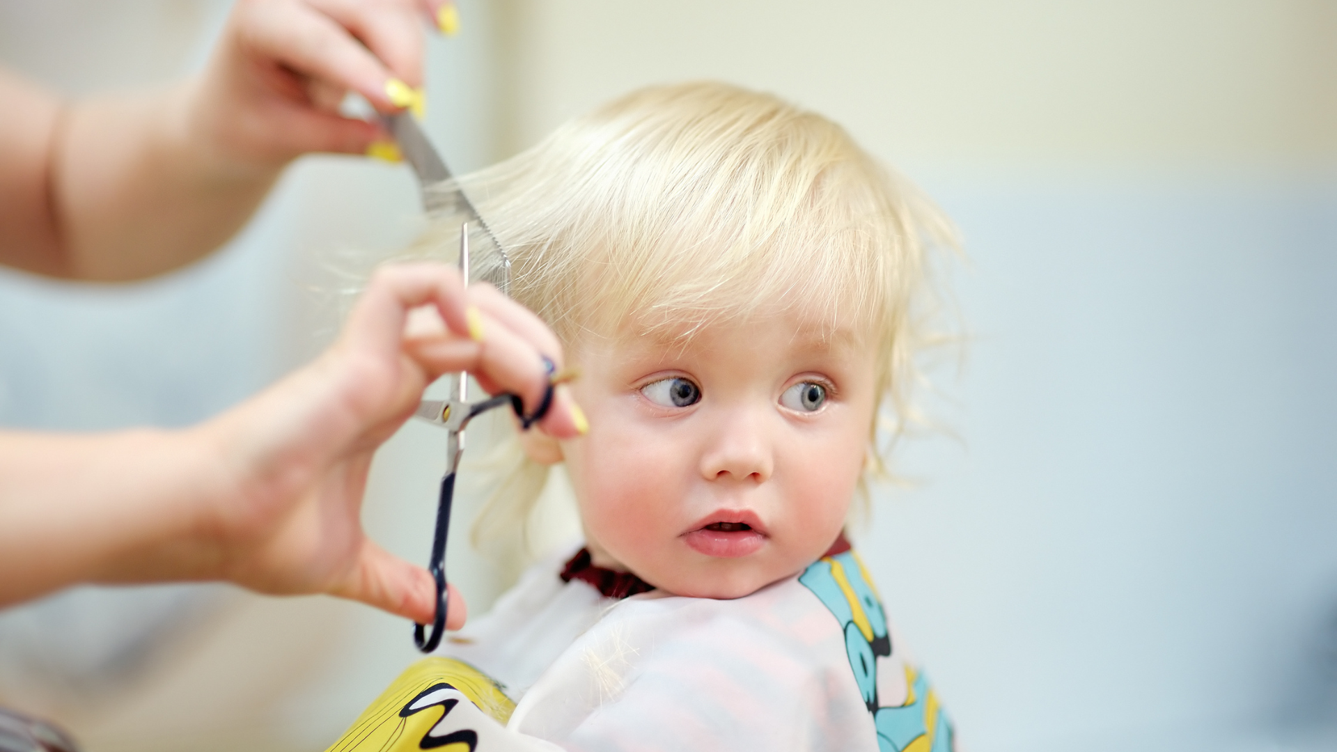 A little girl is getting her hair cut by a hairdresser.