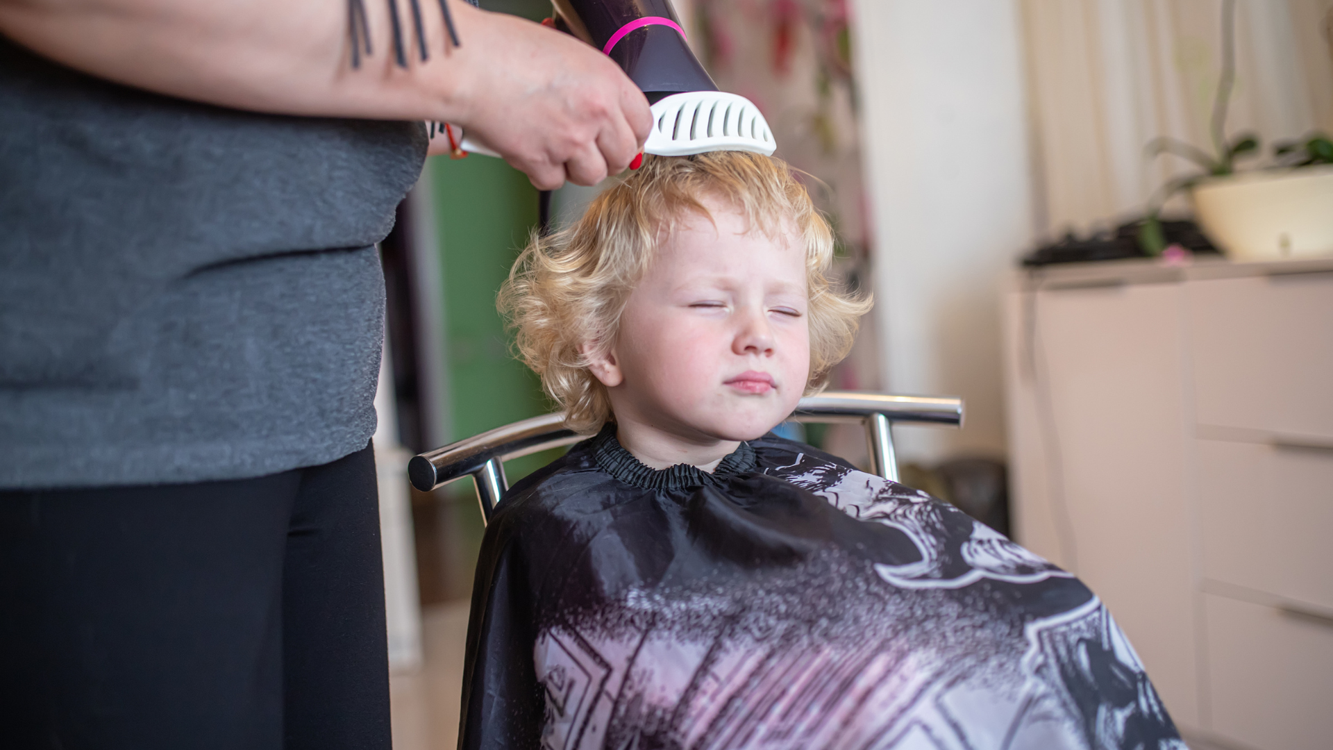 A little boy is getting his hair cut by a hairdresser.