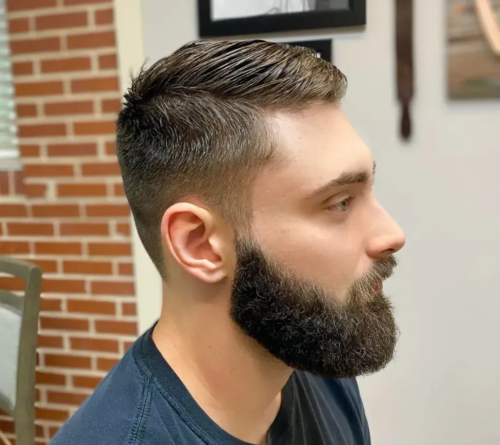 A man with a beard is getting his hair cut at a barber shop.