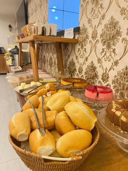 Buffet de café da manhã com diversos tipos de pães, bolos e outros itens alimentícios.