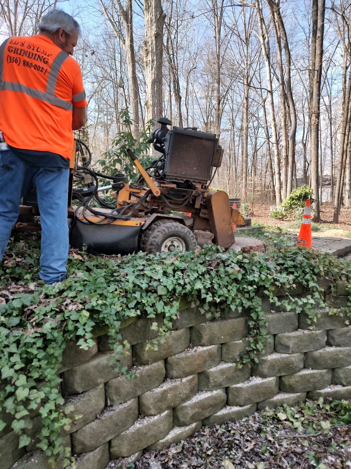 A man is standing next to a stump grinder in the woods.