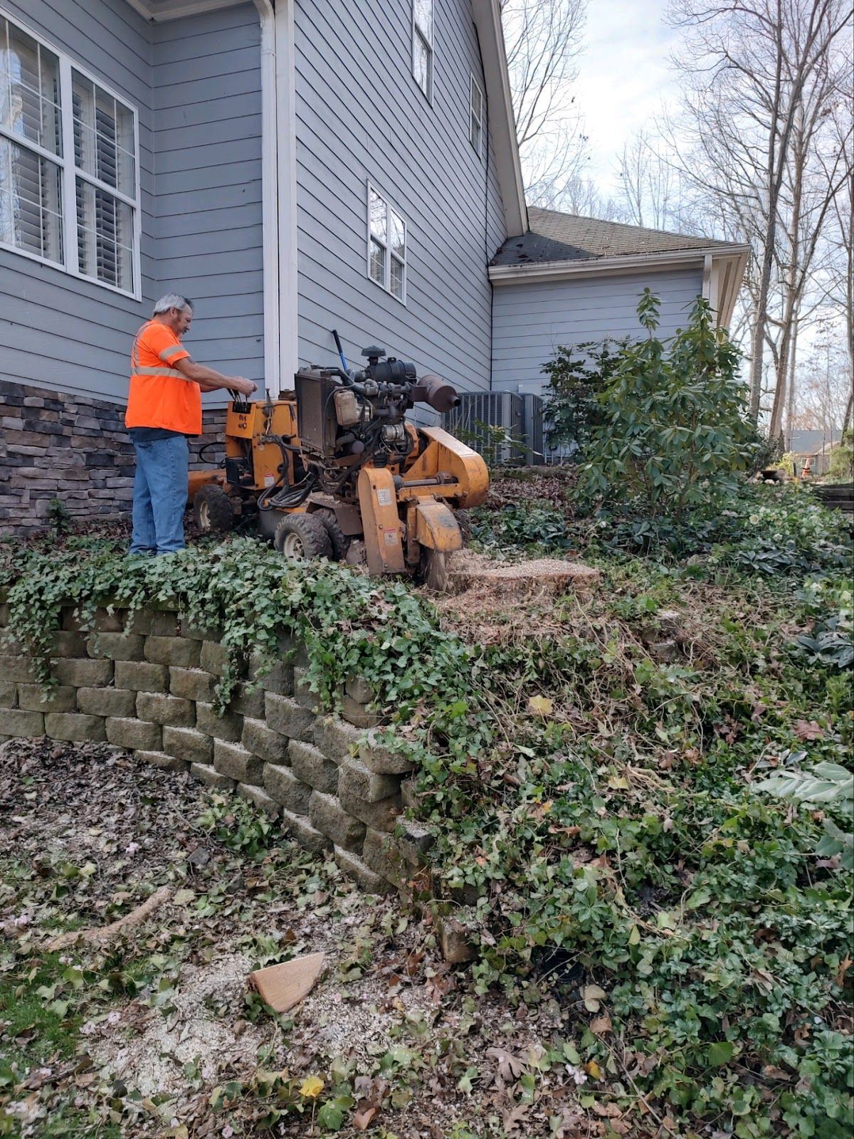 A man is standing next to a stump grinder in front of a house.