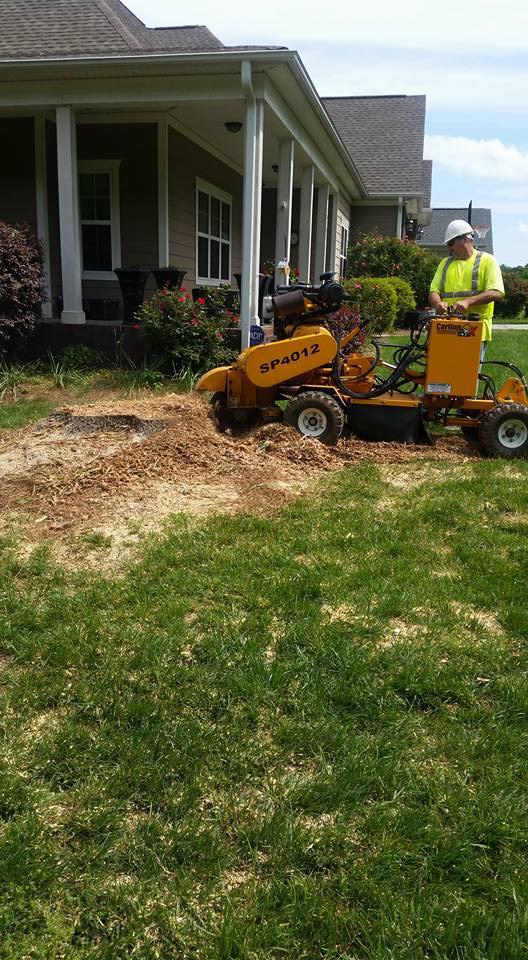 A man is using a stump grinder to remove a tree stump in front of a house.