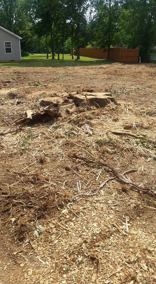A large pile of dirt and branches in a field with a house in the background.