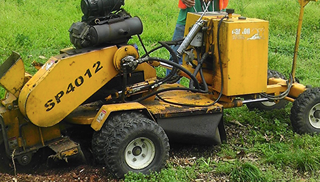 A yellow sp4012 stump grinder is sitting in a grassy field