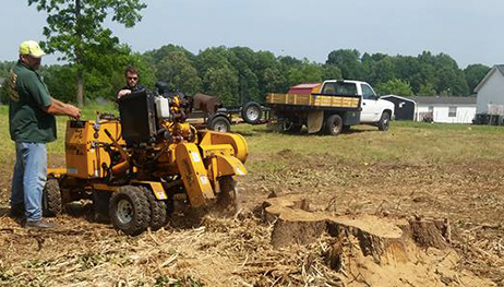 Two men are working on a stump grinder in a field.