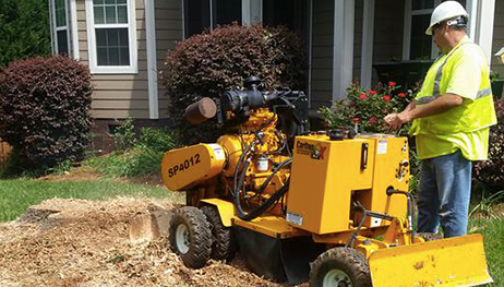 A man is using a machine to remove a tree stump in front of a house.