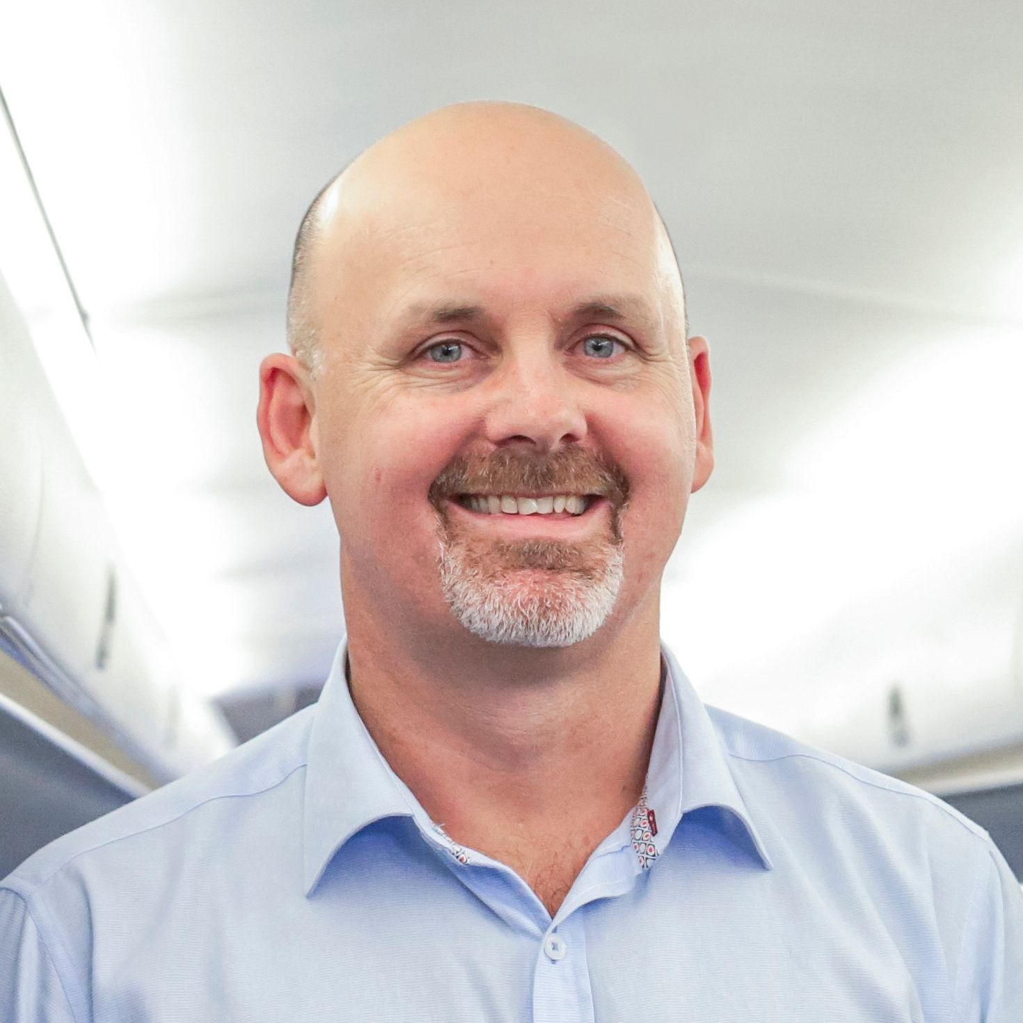 A bald man with a beard is smiling for the camera while wearing a blue shirt.