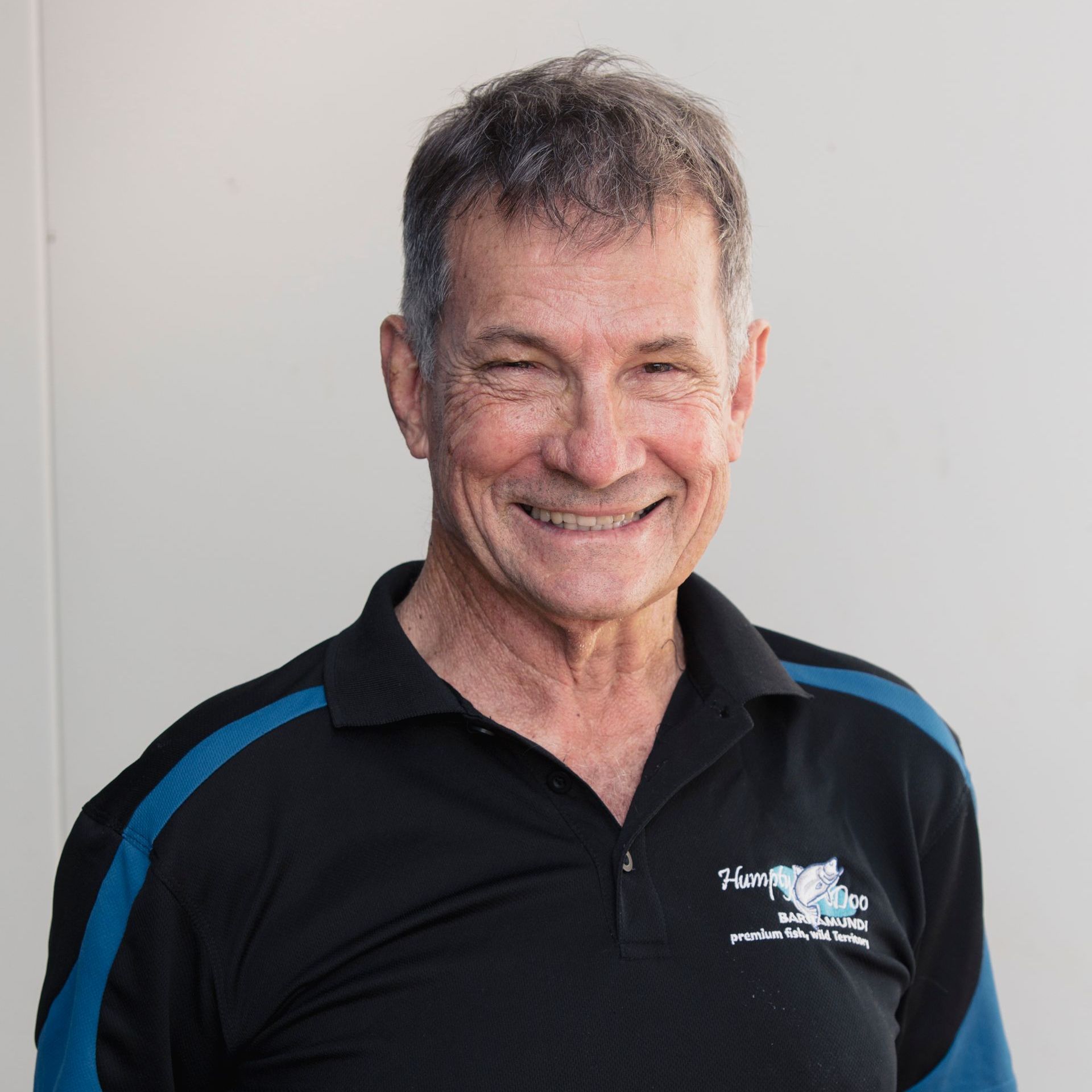 A man wearing a black and blue shirt is smiling for the camera.