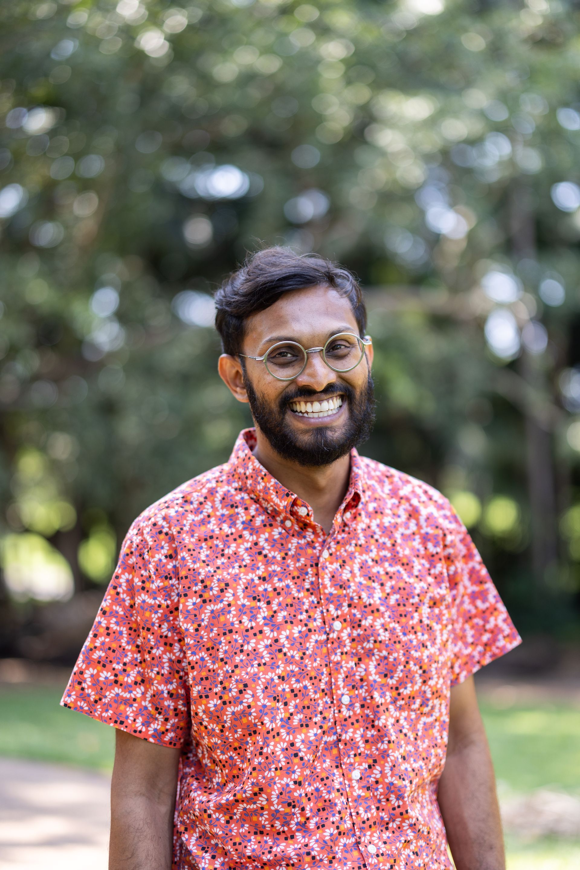 A man with a beard and glasses is wearing a red shirt and smiling.