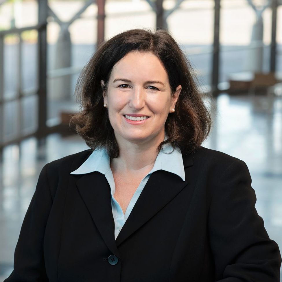 A woman in a black jacket and blue shirt smiles for the camera