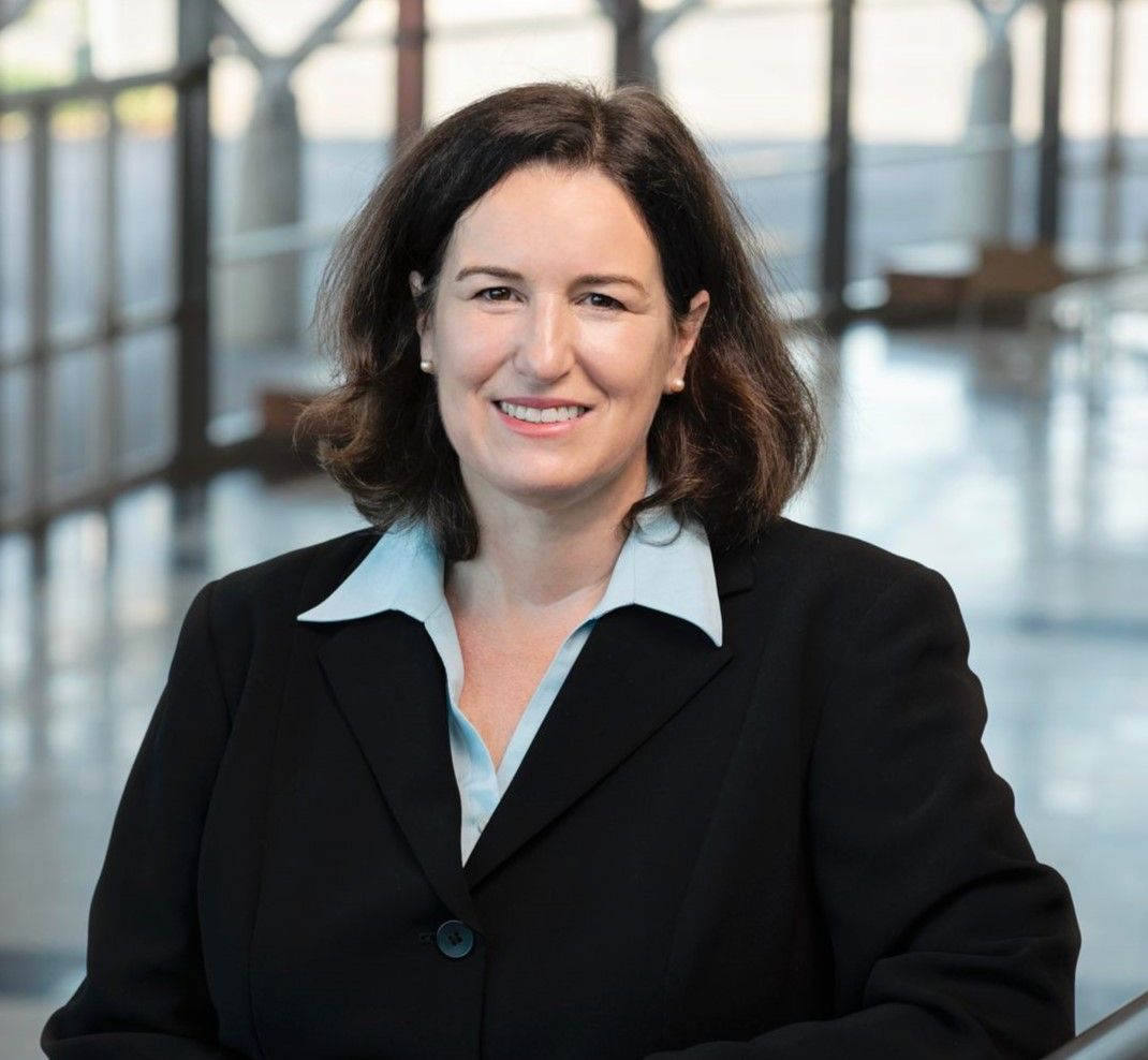 A woman in a black jacket and blue shirt is smiling for the camera.