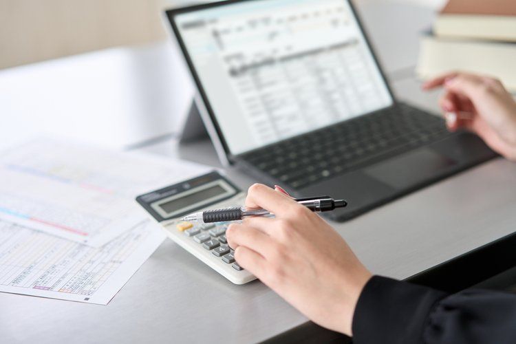 A person is using a calculator in front of a laptop computer.