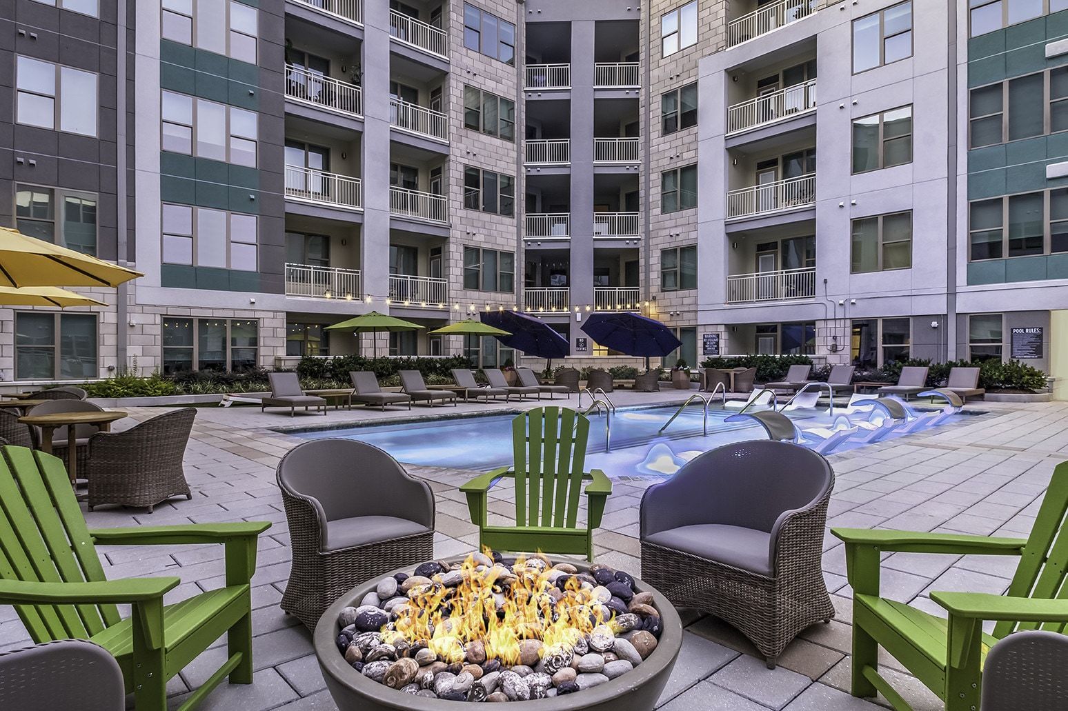 Courtyard with pool, lounge chairs, fire pit, and apartment building in the background.