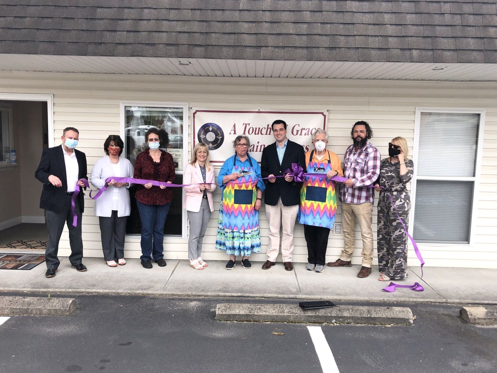 A group of people are cutting a purple ribbon in front of a building.