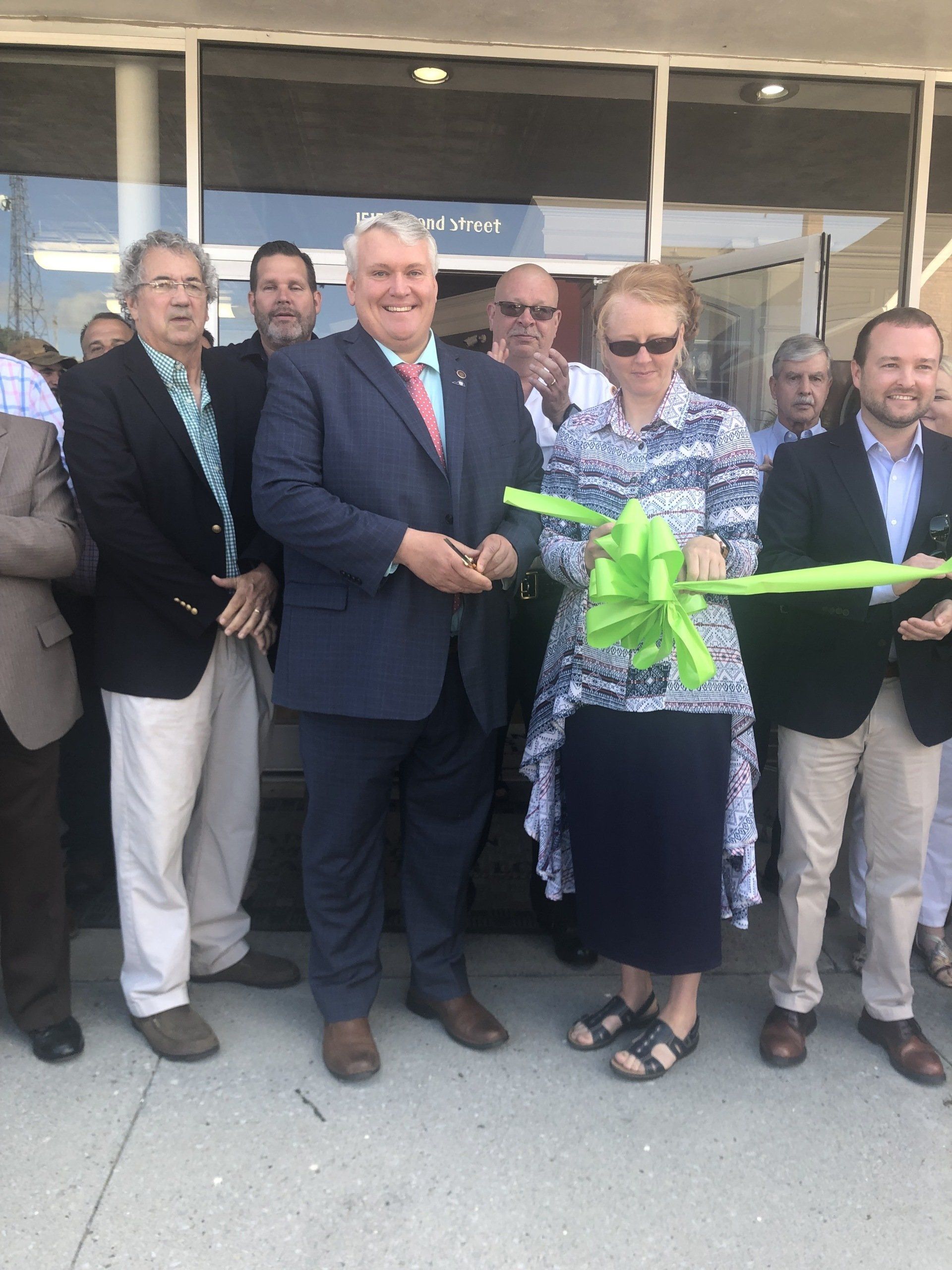A woman is cutting a green ribbon in front of a group of people