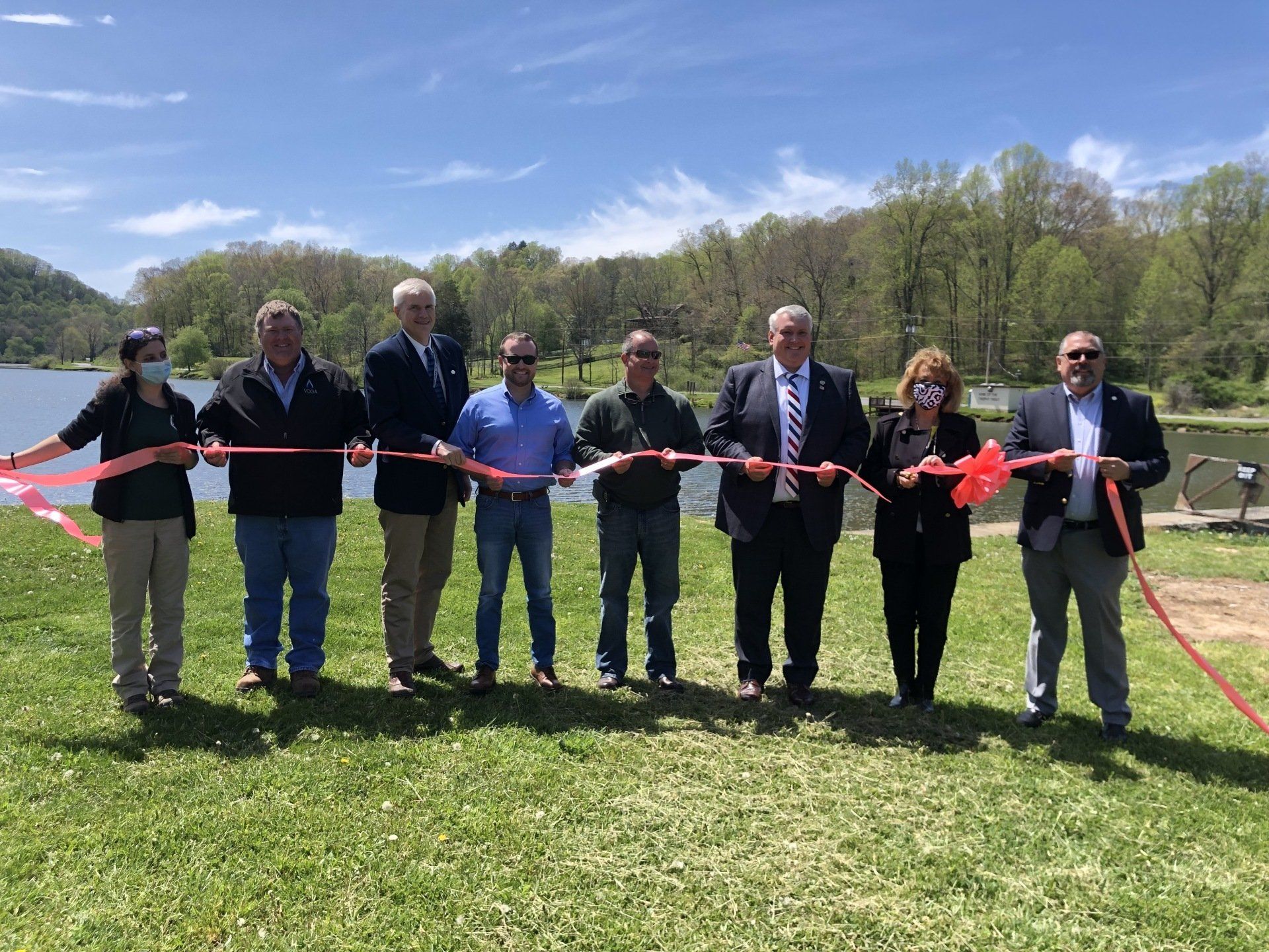 A group of people are cutting a red ribbon in a park.