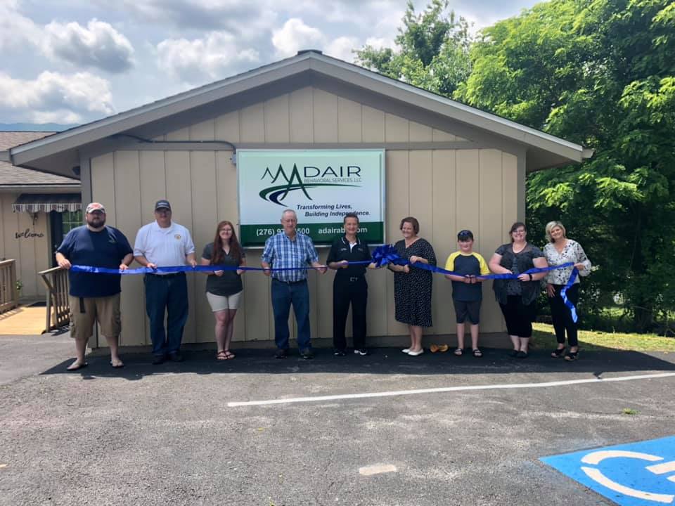 A group of people are cutting a blue ribbon in front of a building.