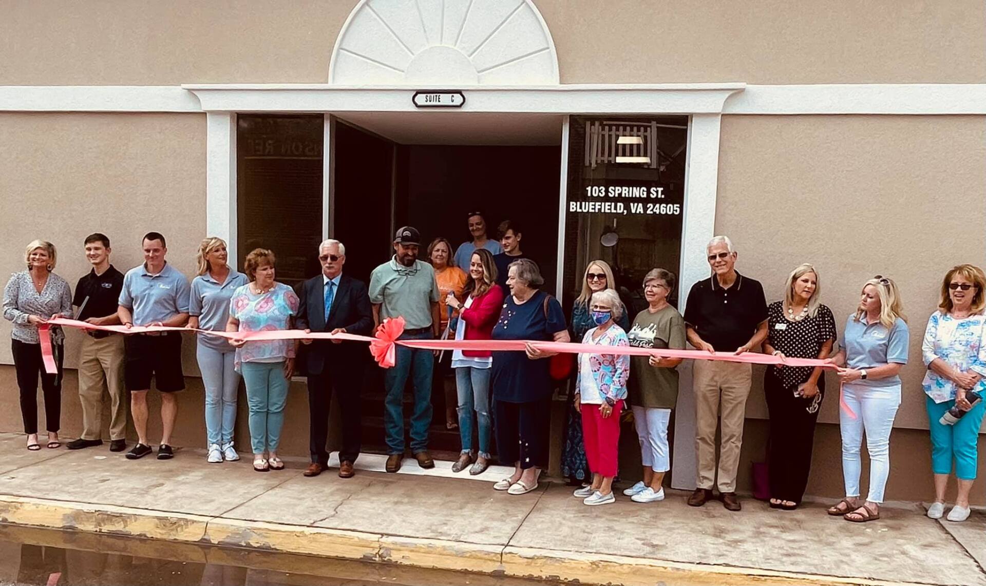 A group of people are standing in front of a building cutting a red ribbon.
