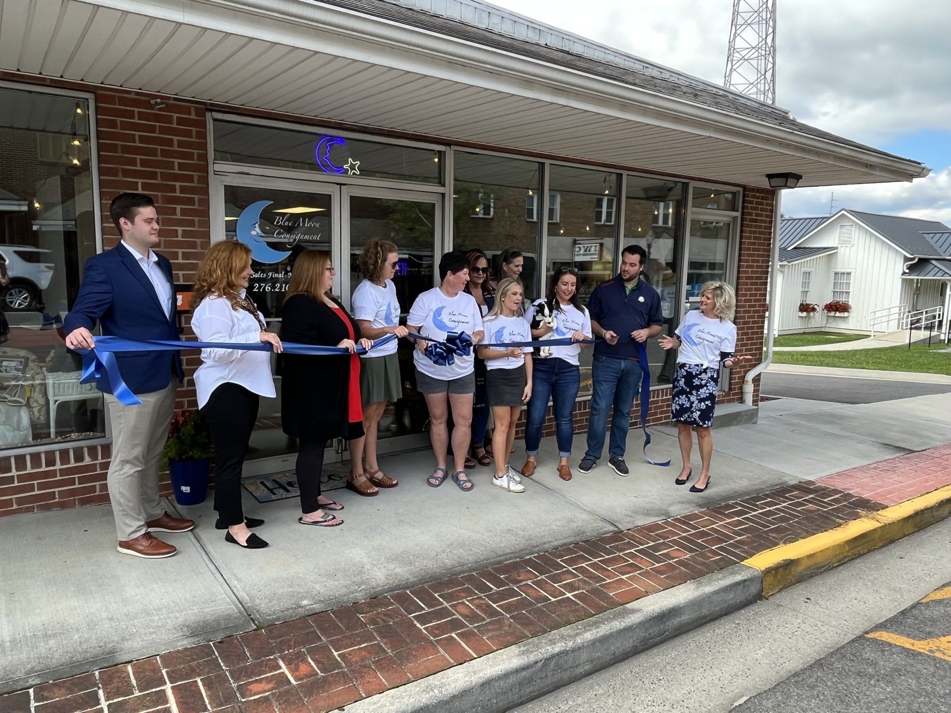 A group of people are cutting a blue ribbon in front of a building.