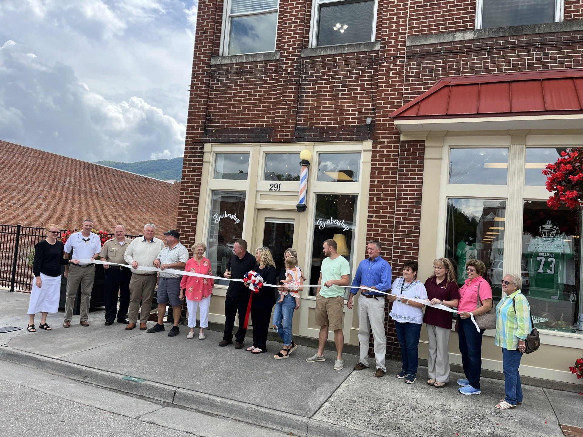A group of people are standing in front of a brick building cutting a ribbon.
