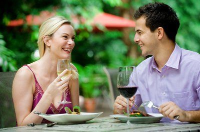 A man and a woman are sitting at a table eating and drinking wine.