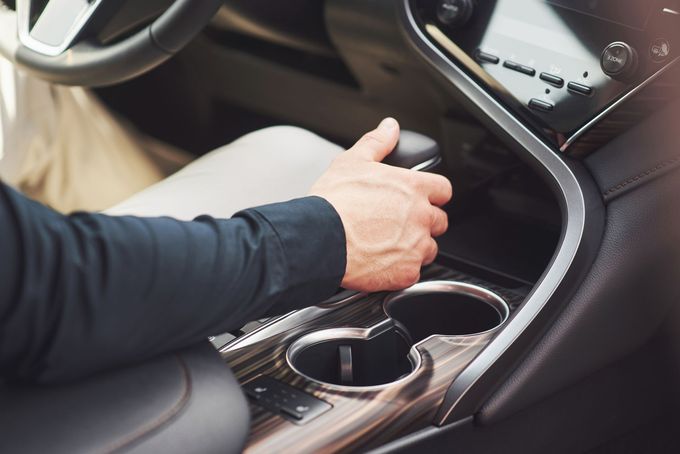 Mano che gira la manopola di controllo della console centrale di un'auto vicino ai portabicchieri e alla leva del cambio