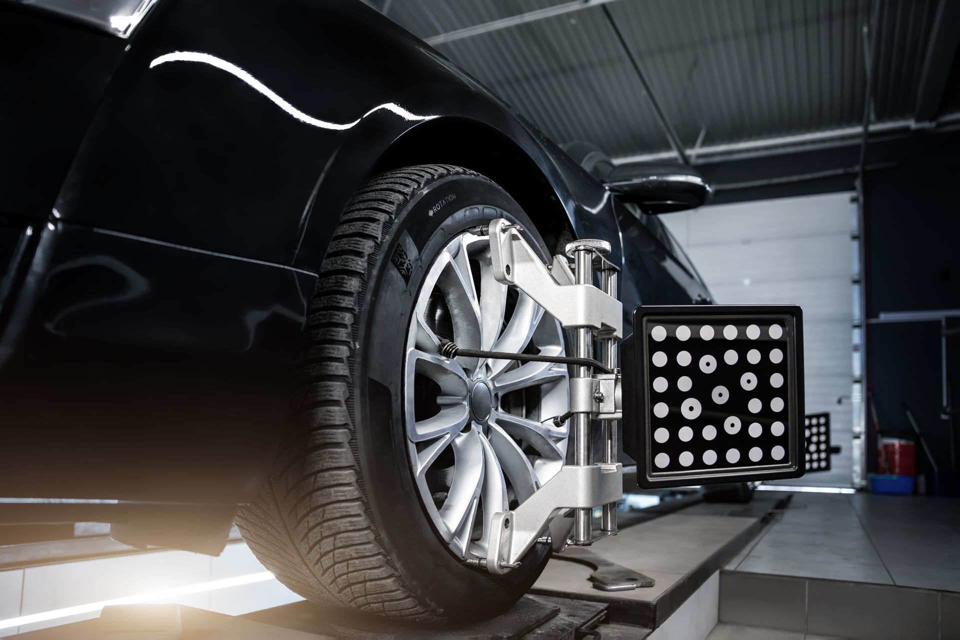 Car wheel on alignment rig in a garage, with a sensor target mounted beside the tire.
