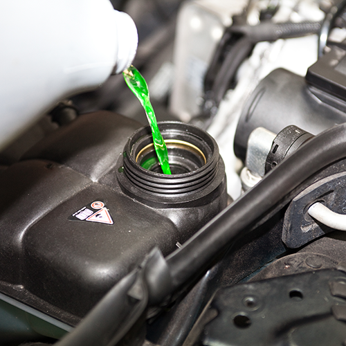 Green coolant pouring into a car’s engine reservoir under the hood