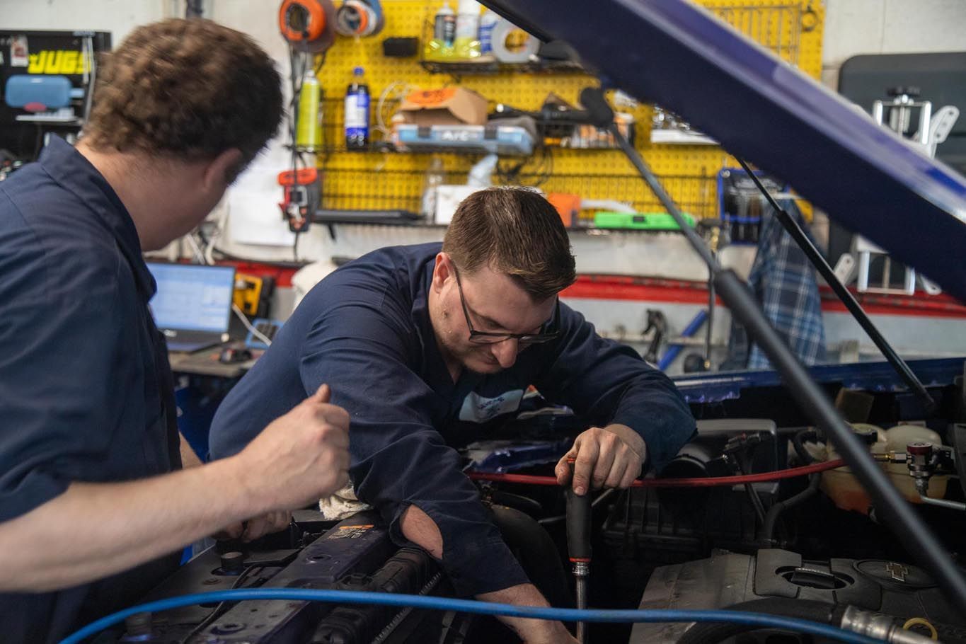 Hand using a wrench to tighten engine parts in a car repair shop