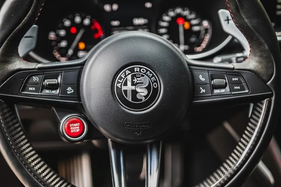 Alfa Romeo steering wheel with dashboard gauges and red start button in a car interior