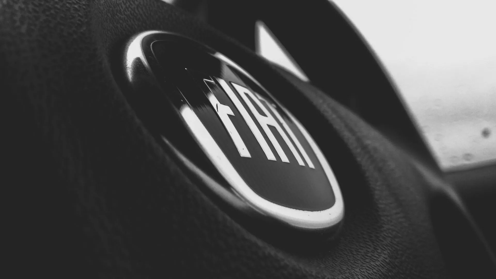 Close-up of the Fiat logo on a car steering wheel in black and white.