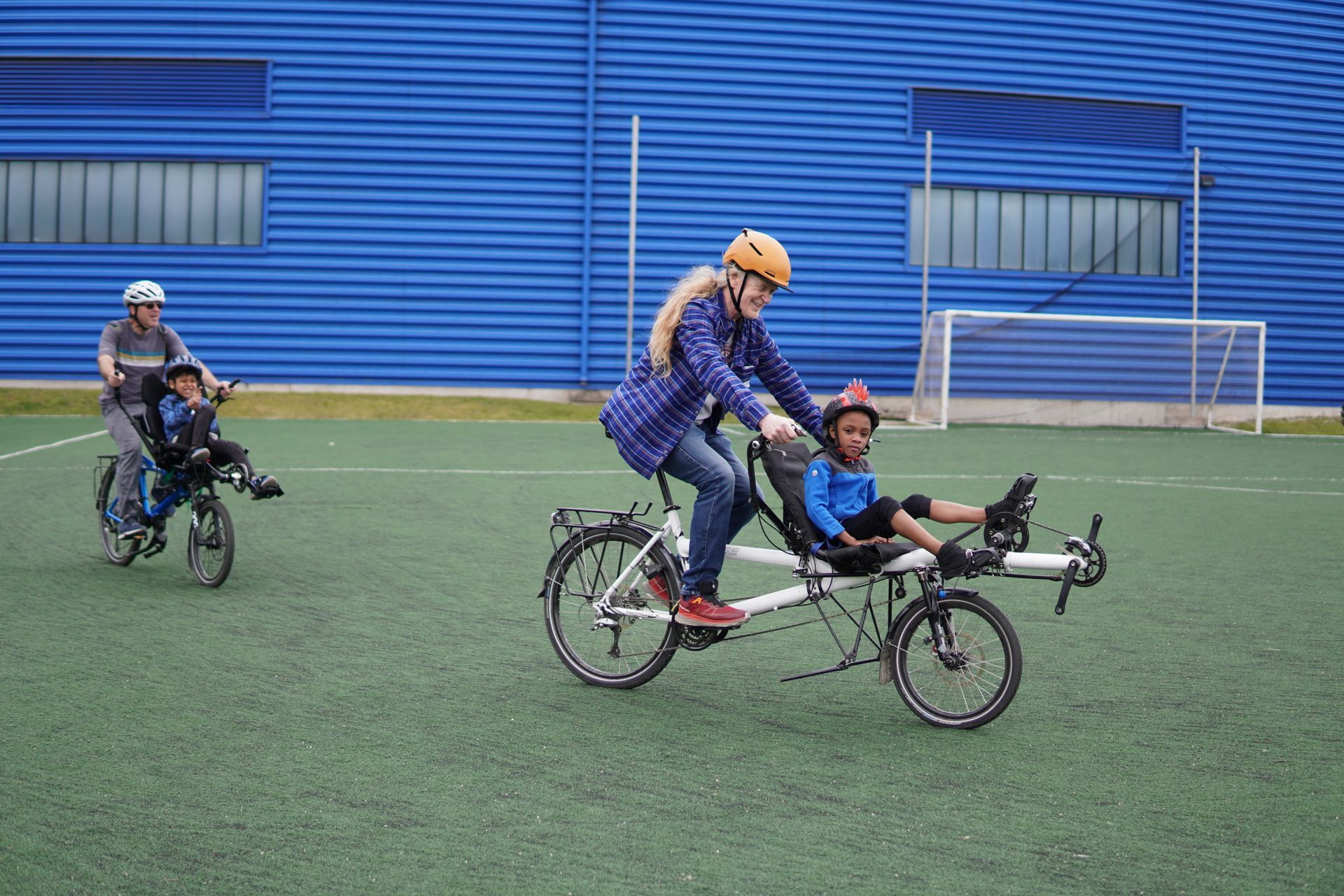 Two attendees ride adaptive bikes with the support of volunteers from Out Our Front Door